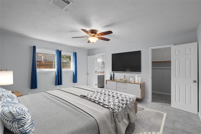 bedroom featuring a walk in closet, a textured ceiling, ceiling fan, connected bathroom, and a closet