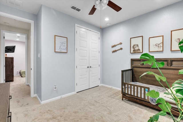 carpeted bedroom with ceiling fan, a crib, and a closet