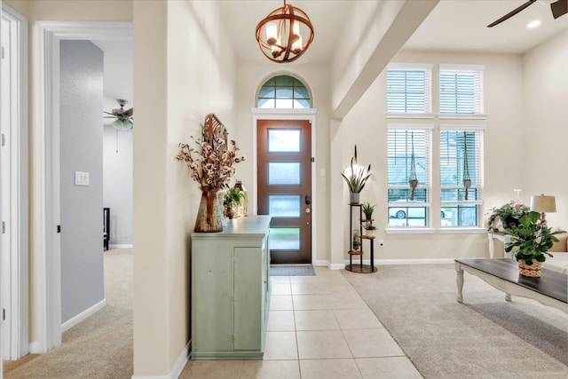 carpeted entryway with a towering ceiling and ceiling fan with notable chandelier