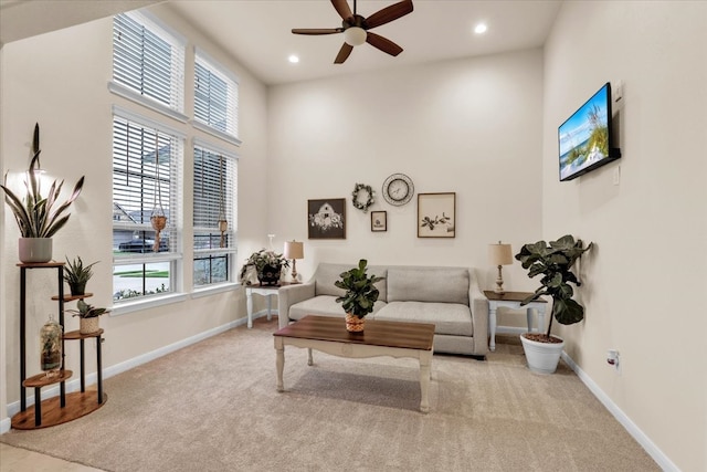 living area with light carpet, a towering ceiling, and ceiling fan