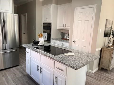 kitchen with hardwood / wood-style floors, a center island, white cabinets, light stone countertops, and stainless steel appliances