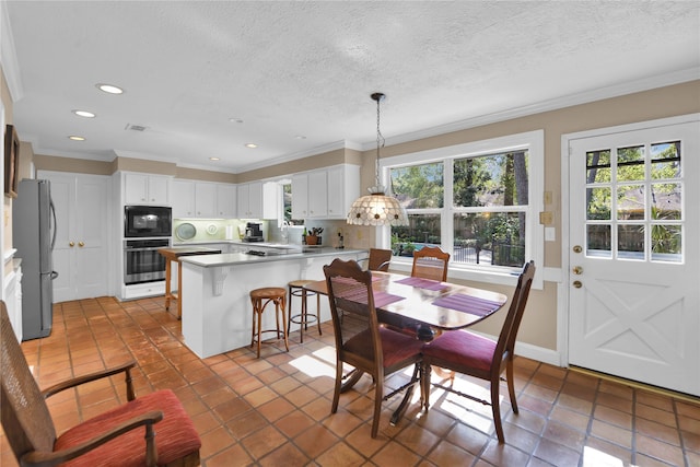 tiled dining room featuring a healthy amount of sunlight, a textured ceiling, and ornamental molding