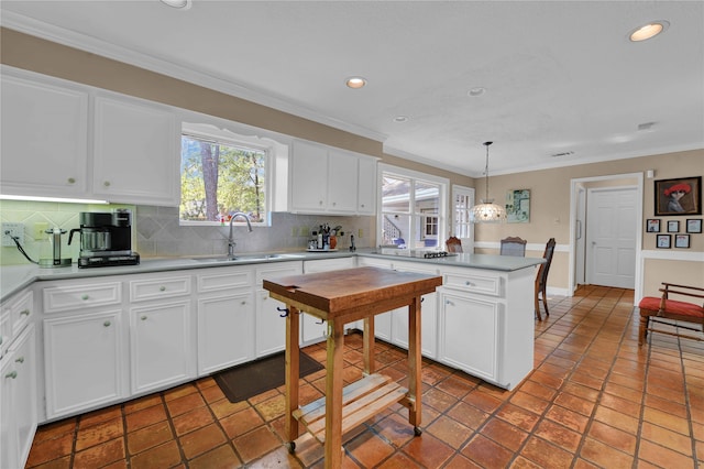 kitchen featuring decorative backsplash, ornamental molding, sink, white cabinets, and hanging light fixtures