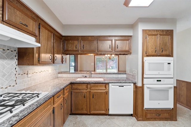 kitchen with tasteful backsplash, white appliances, sink, light tile patterned floors, and a notable chandelier