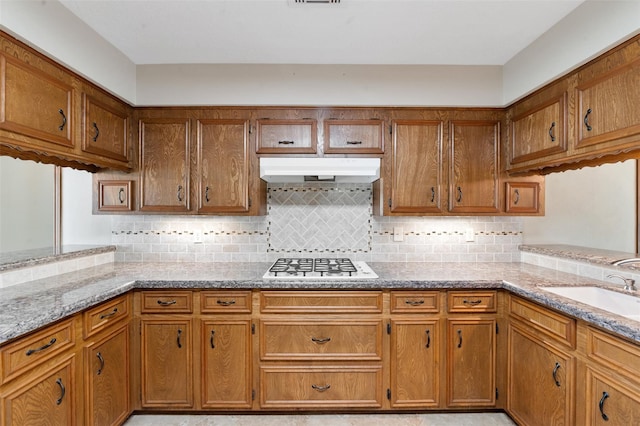 kitchen featuring decorative backsplash, light stone countertops, stainless steel gas cooktop, and sink