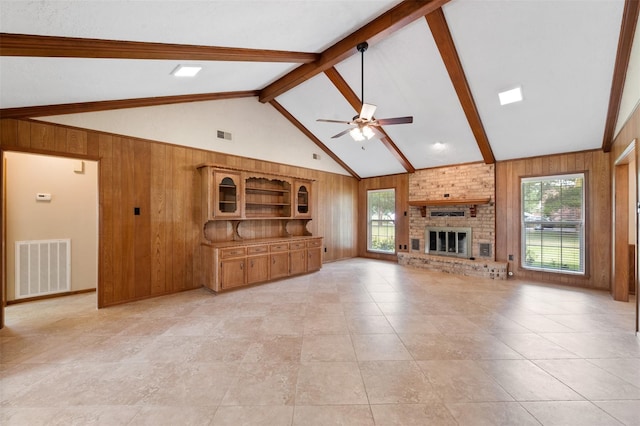 unfurnished living room with wooden walls, beamed ceiling, and a brick fireplace