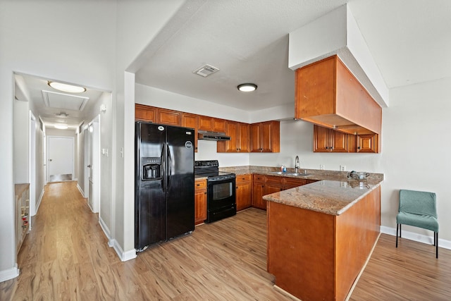 kitchen with visible vents, a peninsula, light wood-style floors, brown cabinetry, and black appliances