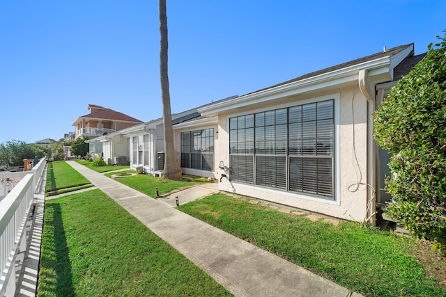 rear view of house with a yard, fence, central AC unit, and stucco siding