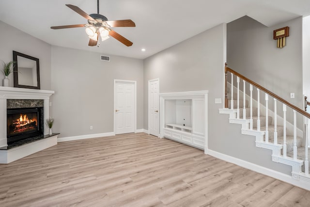 unfurnished living room featuring a high end fireplace, light hardwood / wood-style floors, and ceiling fan