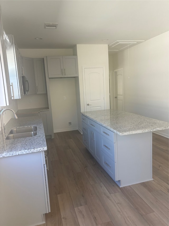 kitchen featuring hardwood / wood-style floors, a kitchen island, light stone counters, and sink