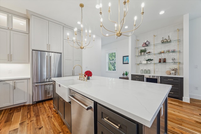 kitchen featuring light stone countertops, light wood-type flooring, stainless steel appliances, sink, and a center island with sink