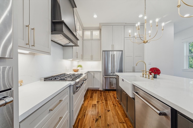 kitchen with high quality appliances, premium range hood, sink, decorative light fixtures, and light hardwood / wood-style floors