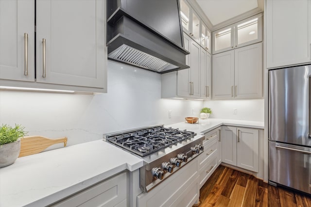 kitchen featuring appliances with stainless steel finishes, premium range hood, light stone counters, dark wood-type flooring, and white cabinets