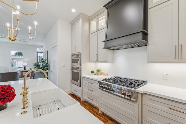 kitchen with light stone counters, custom range hood, stainless steel appliances, dark wood-type flooring, and pendant lighting