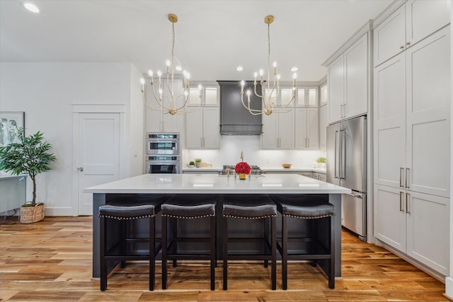 kitchen featuring light hardwood / wood-style floors, premium range hood, an island with sink, and appliances with stainless steel finishes