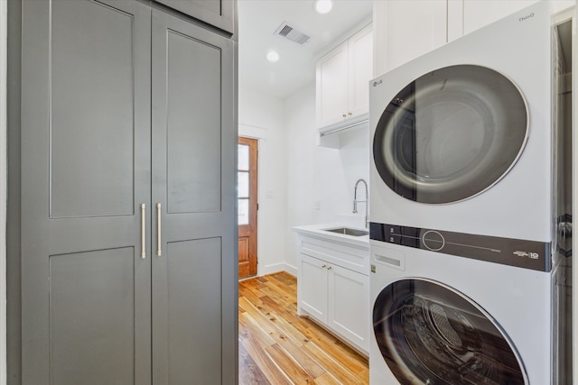 clothes washing area featuring cabinets, light hardwood / wood-style flooring, stacked washer / drying machine, and sink