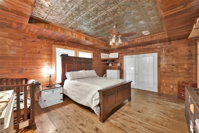 bedroom with ceiling fan, wooden walls, and light hardwood / wood-style flooring