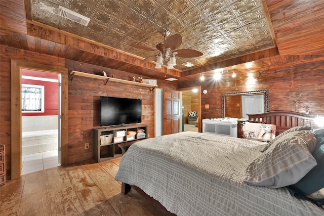 bedroom with hardwood / wood-style flooring, ceiling fan, wooden walls, and connected bathroom