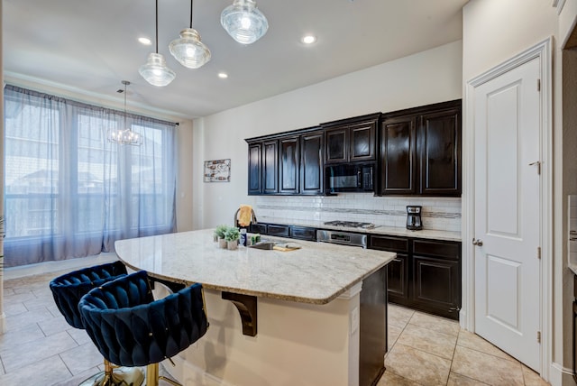 kitchen featuring sink, backsplash, an island with sink, decorative light fixtures, and a kitchen bar