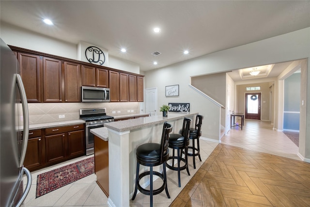 kitchen featuring light stone counters, an island with sink, a breakfast bar area, decorative backsplash, and appliances with stainless steel finishes