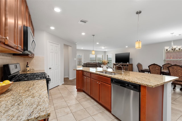 kitchen with appliances with stainless steel finishes, tasteful backsplash, light stone counters, decorative light fixtures, and an island with sink