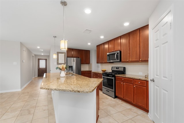 kitchen with hanging light fixtures, stainless steel appliances, light stone counters, a center island with sink, and light tile patterned flooring