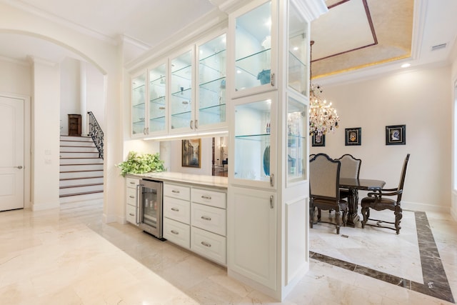 kitchen with white cabinets, a notable chandelier, ornamental molding, and wine cooler