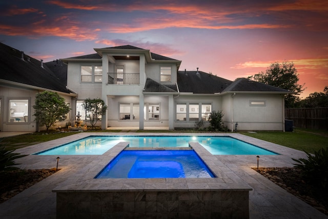 back house at dusk featuring a balcony, cooling unit, and a pool with hot tub