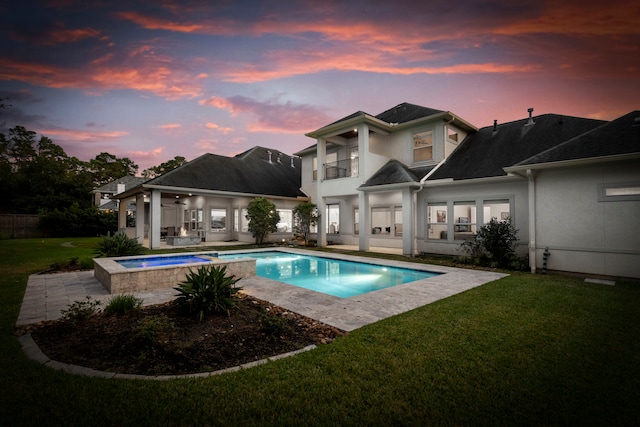 pool at dusk with an in ground hot tub, a patio area, and a lawn