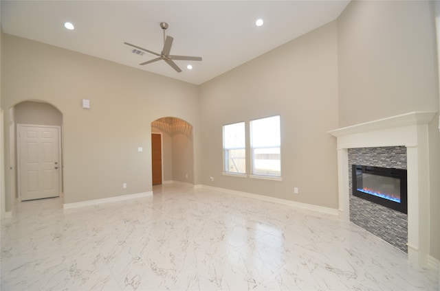 unfurnished living room with a high ceiling, ceiling fan, and a tiled fireplace