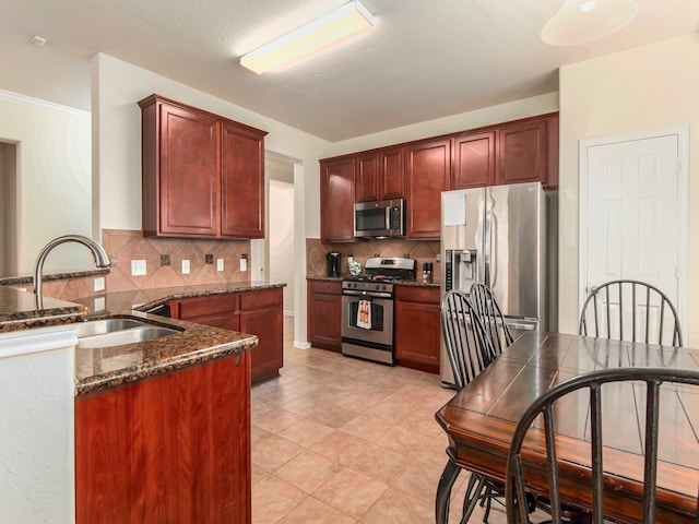 kitchen with kitchen peninsula, tasteful backsplash, dark stone counters, stainless steel appliances, and sink