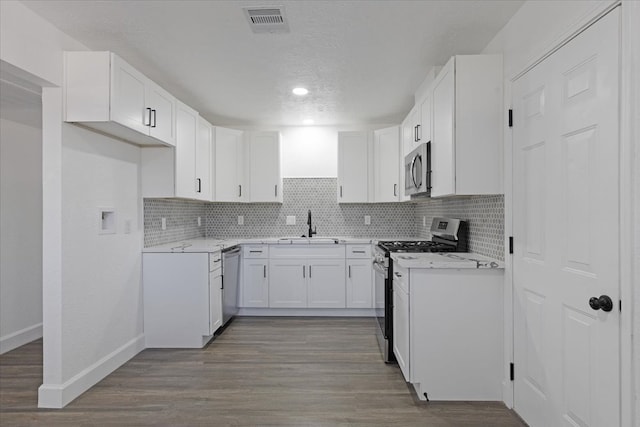 kitchen with white cabinets, sink, decorative backsplash, appliances with stainless steel finishes, and wood-type flooring