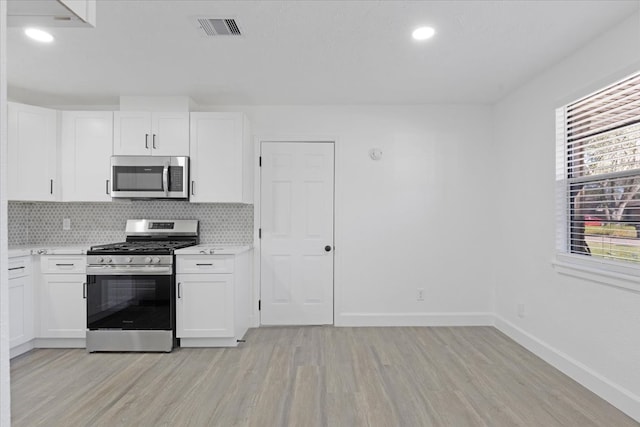 kitchen with backsplash, white cabinets, stainless steel appliances, and light hardwood / wood-style floors