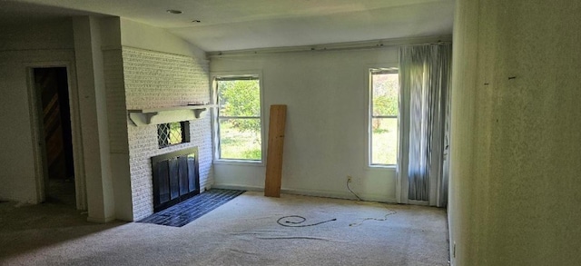 unfurnished room with carpet flooring, lofted ceiling, a wealth of natural light, and a brick fireplace