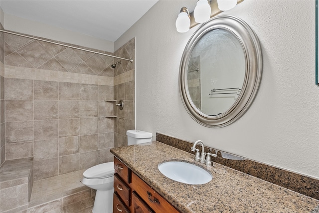 bathroom with tiled shower, vanity, and toilet