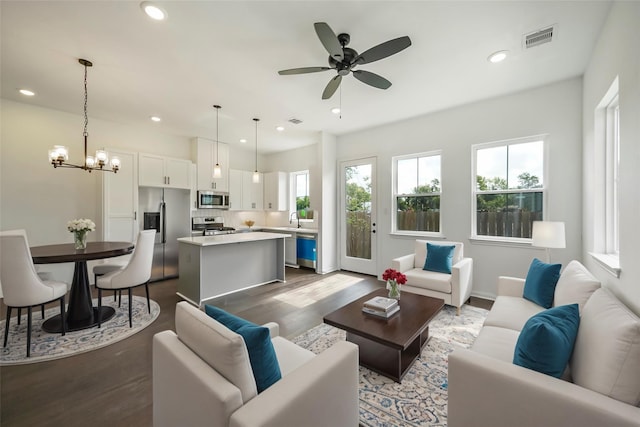 living room featuring ceiling fan with notable chandelier, sink, and dark wood-type flooring