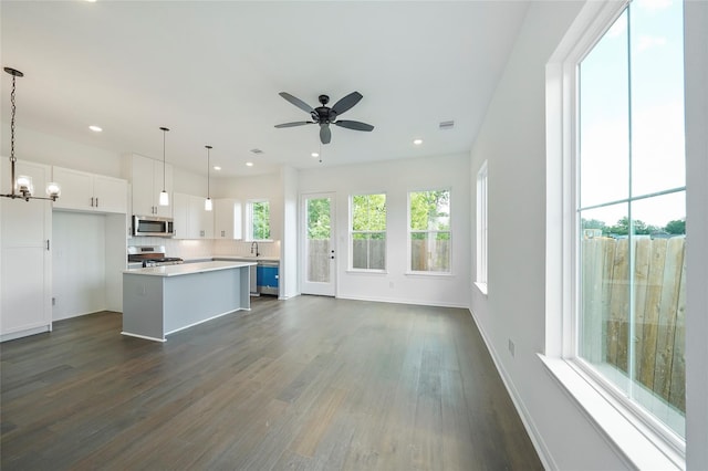 kitchen featuring white cabinetry, a center island, dark wood-type flooring, hanging light fixtures, and appliances with stainless steel finishes