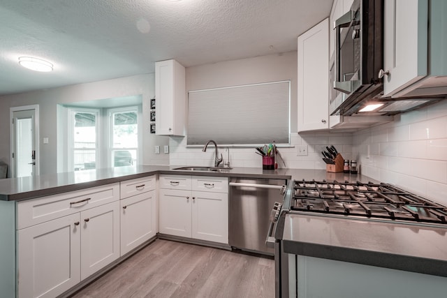 kitchen featuring sink, white cabinetry, light hardwood / wood-style floors, kitchen peninsula, and stainless steel appliances