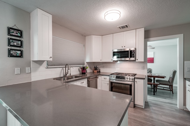 kitchen with white cabinetry, sink, stainless steel appliances, kitchen peninsula, and light hardwood / wood-style floors