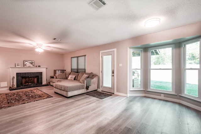 living room featuring a brick fireplace, ceiling fan, a textured ceiling, and light wood-type flooring