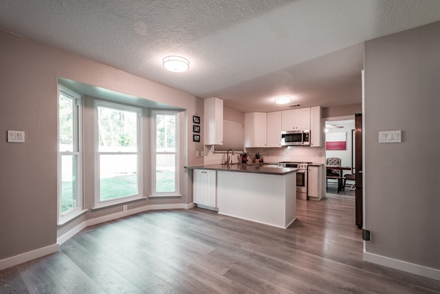 kitchen featuring kitchen peninsula, appliances with stainless steel finishes, a textured ceiling, hardwood / wood-style flooring, and white cabinetry