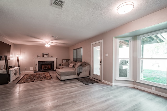 living room featuring a fireplace, a textured ceiling, light hardwood / wood-style flooring, and ceiling fan