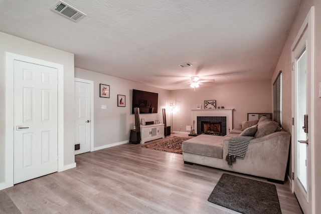 living room with ceiling fan, light hardwood / wood-style floors, a textured ceiling, and a brick fireplace