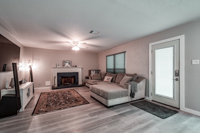 living room with a brick fireplace, ceiling fan, a textured ceiling, and light wood-type flooring