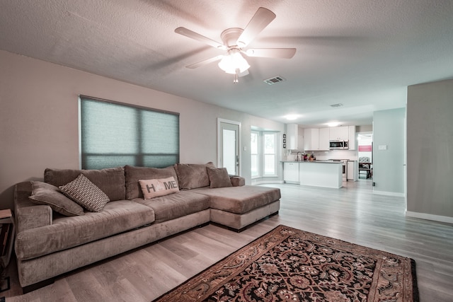 living room featuring a textured ceiling, light hardwood / wood-style floors, and ceiling fan