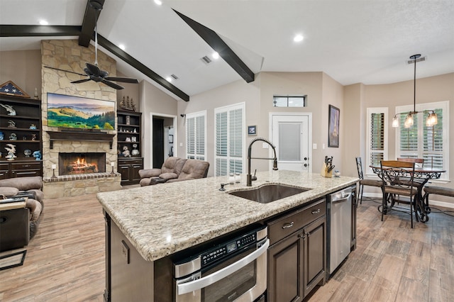 kitchen with sink, a stone fireplace, light hardwood / wood-style flooring, pendant lighting, and a kitchen island with sink