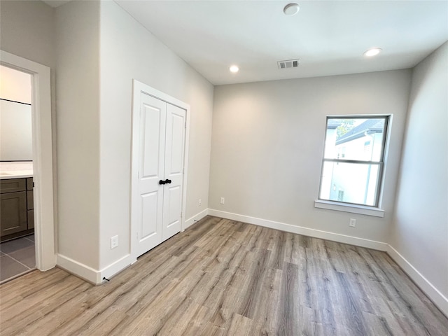 unfurnished bedroom featuring connected bathroom, light hardwood / wood-style flooring, and a closet