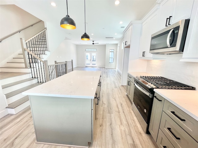 kitchen with appliances with stainless steel finishes, decorative light fixtures, white cabinets, light hardwood / wood-style floors, and a kitchen island