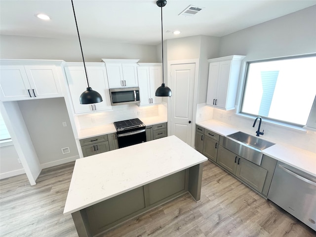 kitchen with white cabinets, stainless steel appliances, decorative light fixtures, and a kitchen island