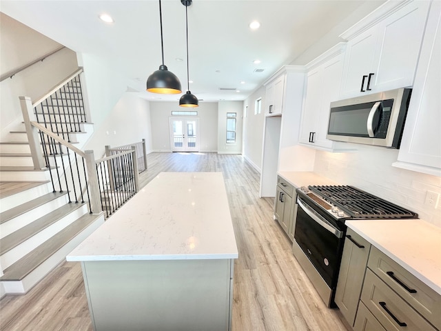 kitchen featuring white cabinets, hanging light fixtures, light wood-type flooring, and appliances with stainless steel finishes